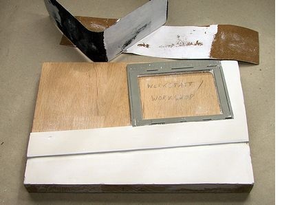 Grundplatte mit abgeschliffener Gipsschicht neben 2 Streifen Schleifpapier