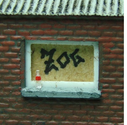 Colaflasche auf der Fensterbank des Schuppens, dahinter ein Graffiti auf der Sperrholzplatte